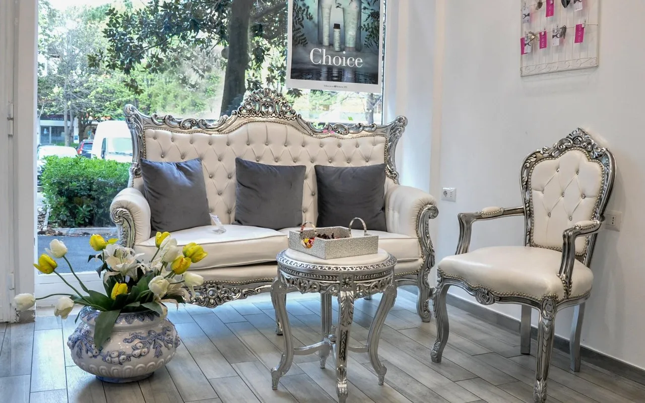 Il salotto d'attesa di Love Hair: divano capitonné bianco e argento, poltrona barocca e tulipani davanti alla vetrata
